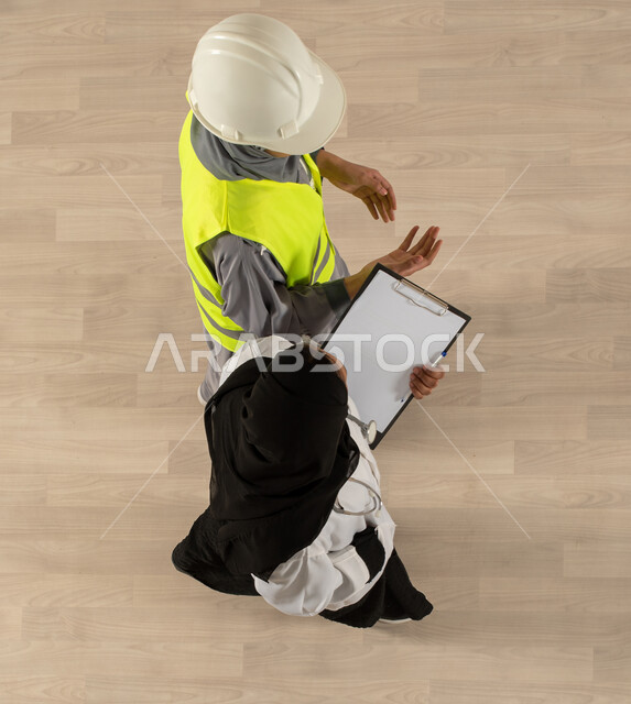 The profession of medicine and health care, wearing a medical uniform, an overhead vertical image of two Saudi Arab Gulf women, Saudi employment and job opportunities, the profession of architecture, wearing a work protection jacket and helmet, work discu