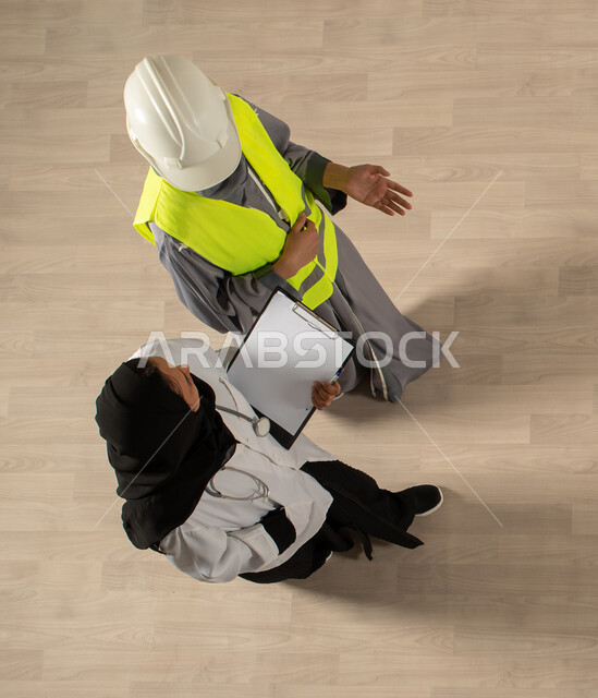 مهنة الطب والرعاية الصحية، مهنة الهندسة المعمارية، صورة عامودية علوية لسيدتان عربيتان خليجيتان سعوديتان، العمالة السعودية وفرص العمل، ارتداء سترة وخوذة الحماية الخاصة بالعمل، ارتداء الزي الطبي، نقاشات وحوارات عمل، مهن ووظائف سعودية