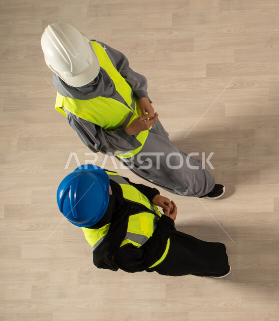 صورة عامودية علوية لمهندستان معماريتان عربيتان خليجيتان سعوديتان، ارتداء سترة وخوذة الحماية الخاصة بالعمل، نقاشات وحوارات عمل، مهنة الهندسة المعمارية، العمالة السعودية وفرص العمل، مهن ووظائف سعودية