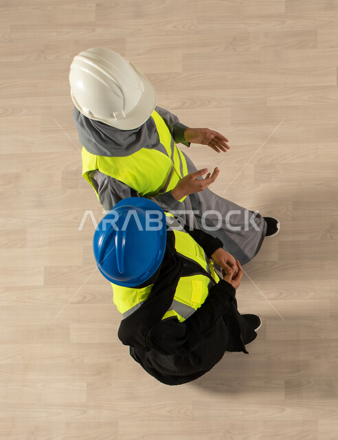 Saudi employment and job opportunities, an overhead vertical image of two Saudi Arab Gulf architects, wearing a work protection jacket and helmet, business discussions and dialogues, the architecture profession, Saudi professions and jobs