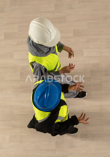 ارتداء سترة وخوذة الحماية الخاصة بالعمل، صورة عامودية علوية لمهندستان معماريتان عربيتان خليجيتان سعوديتان، نقاشات وحوارات عمل، مهنة الهندسة المعمارية، العمالة السعودية وفرص العمل، مهن ووظائف سعودية