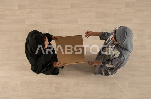 A reliable and successful shipping and delivery process, a woman receiving the order from the delivery representative, an overhead vertical image of two Saudi Arabian Gulf women wearing traditional Saudi clothing, delivery of orders to customers, express 