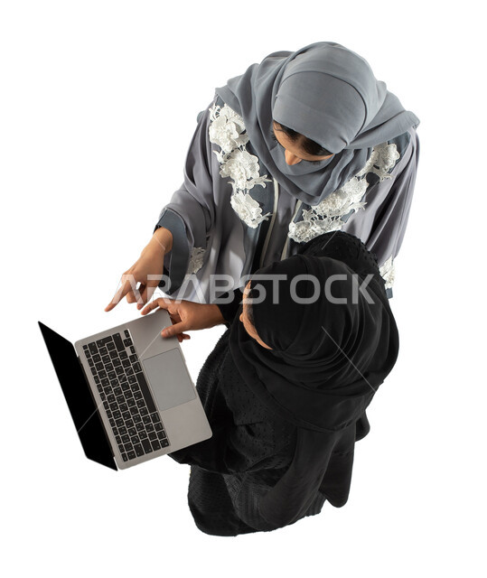 زملاء عمل في شركة سعودية، صورة علوية عامودية لسيدتان اعمال عربيتان خليجيتان سعوديتان داخل مقر الشركة، استخدام جهاز الحاسوب المحمول، متابعة ومناقشة وتنظيم الاعمال، فريق عمل سعودي، مهن ووظائف سعودية، خلفية بيضاء