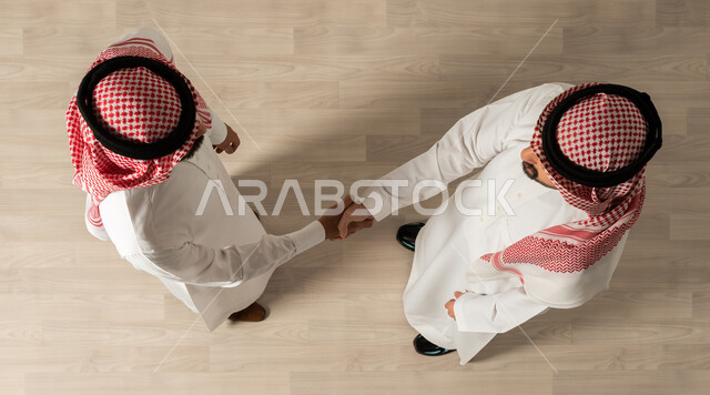 تحقيق اهداف الشركه ، التصافح داخل الشركة ،عقد صفقات جديده  ، صورة علوية عامودية لرجلان عربيان خليجيان سعوديان يرتديان الزي السعودي التقليدي , مهن ووظائف سعودية ، اجتماع عمل , اتفاقيات عمل ناجحه