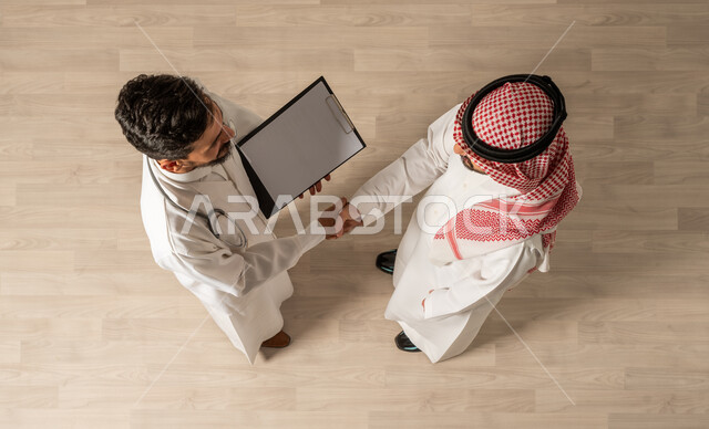 كتابة وتسجيل التقارير الطبيه والحالات الصحيه . مفهوم مهنة الطب ، رجل عربي سعودي خليجي يصافح طبيب عربي سعودي خليجي ، وظائف عربيه سعوديه خليجيه ، مستشفيات ومراكز صحيه ، التحية والسلام
