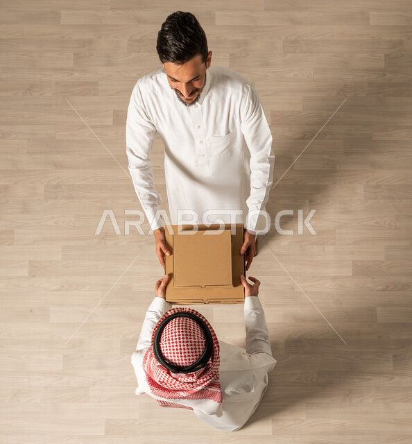  التسوق الالكتروني ، صورة علوية عامودية لرجلان عربيان خليجيان سعوديان يرتديان الزي السعودي التقليدي ، عملية شحن وتوصيل موثوقه, خدمة التوصيل السريع  ، طلبات اونلاين, التسوق الذكي