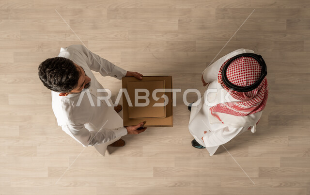 Express delivery service, vertical overhead image of two Saudi Arab Gulf men wearing traditional Saudi clothing, online shopping, online requests, smart shopping, reliable shipping and delivery