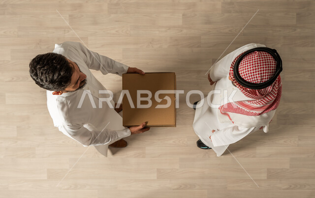 التسوق الذكي, صورة علوية عامودية لرجلان عربيان خليجيان سعوديان يرتديان الزي السعودي التقليدي ، التسوق الالكتروني ، طلبات اونلاين, عملية شحن وتوصيل موثوقه, خدمة التوصيل السريع