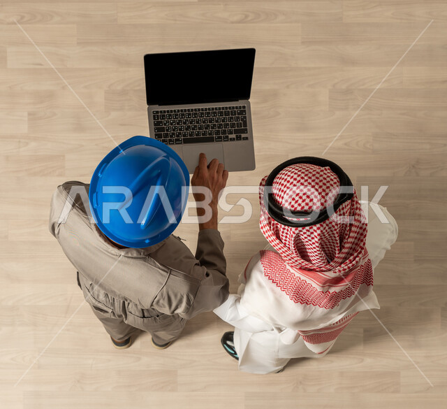 عمل جماعي مشترك ، صورة علوية عمودية لرجلان عربيان خليجيان سعوديان في وظائف مختلفة بالسعودية ، مهنة الهندسة ، مهن ووظائف سعودية، استخدام جهاز الحاسوب المحمول