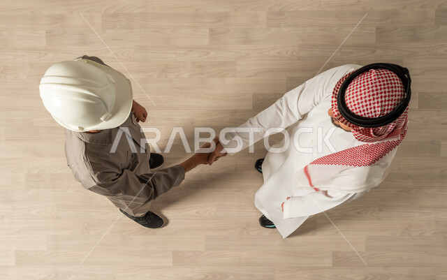 صفقات عمل ناجحه, اتفاقات عمل جديده, مهنة الهندسة المعماريه والمدنيه ، صورة علوية عامودية لرجلان عربيان خليجيان سعوديان في وظائف مختلفة بالسعودية، التصافح داخل الشركة  ، مهن ووظائف سعودية