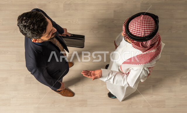 لقاء الأصدقاء ، تعارف وصداقة ،صوره علويه عاموديه لرجل عربي سعودي خليجي يرتدي الزي السعودي التقليدي ورجل عربي يرتدي البدله الرسميه ، انجاز مهام العمل،  حوارات و نقاشات عمل ،مهن ووظائف السعودية