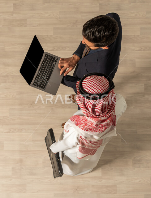  نقاشات عمل ، صوره علويه عاموديه لرجل عربي سعودي خليجي يرتدي الزي السعودي التقليدي  ورجل عربي يرتدي البدله الرسميه , استخدام جهاز الحاسوب المحمول , إنجاز مهام العمل , عمل جماعي مشترك