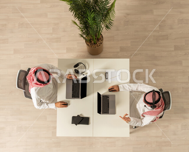 ارتداء سماعة الرأس , العمل في مجال الدعم الفني وخدمة العملاء, استعلامات واستفسارات ، اعمال مكتبيه ،صوره علويه عاموديه لزملاء عمل في مقر الشركة يرتديان الزي السعودي التقليدي ، استخدام جهاز الحاسوب المحمول، انجاز مهام العمل، اعمال مكتبيه ، مهن ووظائف سعوديه