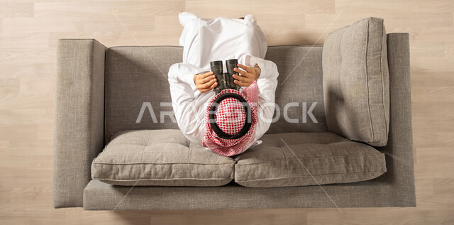 صورة من الاعلى لرجل عربي خليجي سعودي يجلس على الاريكة وينظر من خلال الناظور، التخطيط المستقبلي لفريق الكشافة، الاستكشاف والمغامرة ورؤية الاهداف المستقبلية، امتلاك بيت جديد
