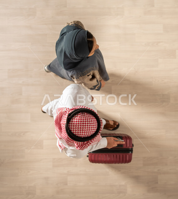 A picture from above of a Saudi Arabian Gulf couple carrying a travel bag and getting ready to spend the summer vacation, traveling on a tourist tour, spending fun family times, a tourist travel trip, tourism and hotel