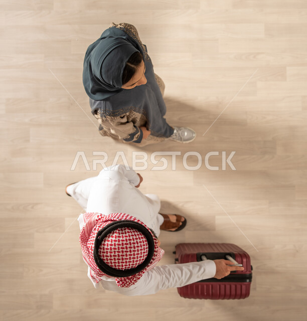 A picture from above of a Saudi Arabian Gulf couple carrying a travel bag and getting ready to spend the summer vacation, traveling on a tourist tour, spending fun family times, a tourist travel trip, tourism and hotel