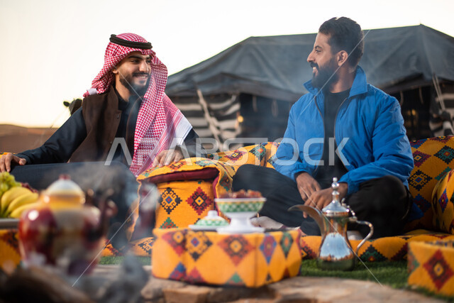 الاستمتاع في قضاء الوقت مع الأصحاب، ارتداء الملابس الشتوية الدافئة، حسن الضيافة والاستقبال، أجواء تخييم شبابية ليلية أمام شعلة الحطب، أصدقاء عربيون خليجيون سعوديون يجلسون أمام النيران المشتعلة في كشتة برية، جلسة بر عربية شعبية، مخيمات سياحية في صحاري السعودية