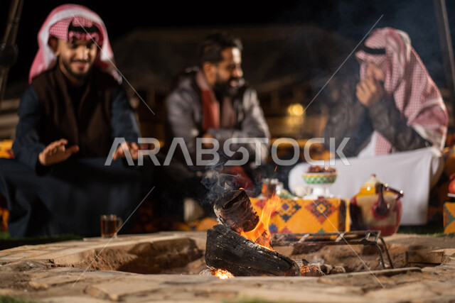 مخيمات سياحية في صحاري السعودية، التدفئة من خلال شعلة النار، حسن الضيافة والاستقبال عند العرب، قضاء أوقات ممتعة مع الأصحاب، أجواء تخييم شبابية ليلية أمام الحطب، أصدقاء عربيون خليجيون سعوديون يجلسون أمام النيران المشتعلة في كشتة برية، جلسة بر عربية شعبية