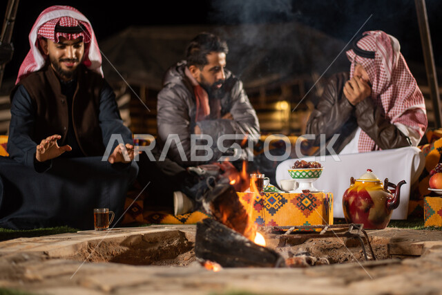 Enjoying spending time with friends, a youth camping atmosphere at night in front of firewood, Saudi Gulf Arab friends sitting in front of burning fires in a wild kashta, a popular Arab bar session, tourist camps in the deserts of Saudi Arabia, heating through the flame of a fire, good hospitality and reception among Arabs.