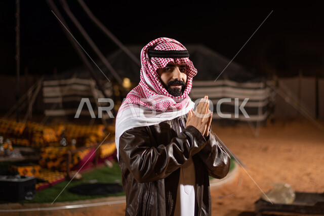 جاكيت جلد بني شتوي سميك، مخيمات سياحية في الصحراء، خيام شعبية في صحاري السعودية، اجواء شتوية ليلية، ايماءات البرد القارس الشديد، رحلة تخييم برية في المملكة، صورة مقربة لرجل عربي خليجي سعودي يرتدي الثوب التقليدي والشماغ مع ملابس الشتاء الدافئة