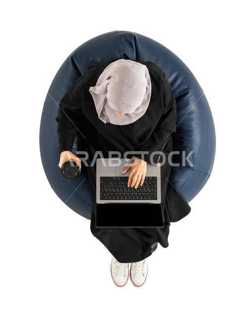 الجلوس على كرسي مريح ، تناول القهوة والمشروبات الساخنة ،بورتريه لصورة علوية عامودية لأمرأة عربية خليجية سعودية تجلس على كرسي ،  استخدام الحاسوب المحمول ، امرأة تمسك بيدها كوب القهوة ، خلفية بيضاء