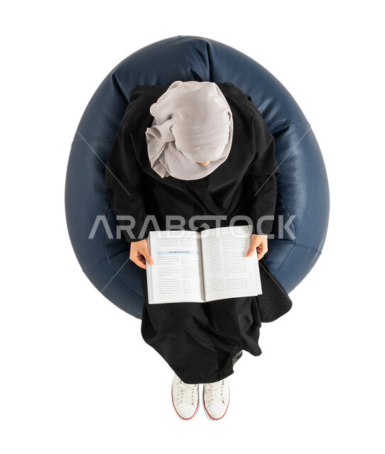 ثقافة القراءة، التعلم والثقافة ، قضاء الوقت بالقراءه،  بورتريه لصورة علوية عامودية لسيدة عربية خليجية سعودية تجلس على كرسي مريح وتحمل بيدها جريدة ورقية ، المعرفة، خلفية بيضاء