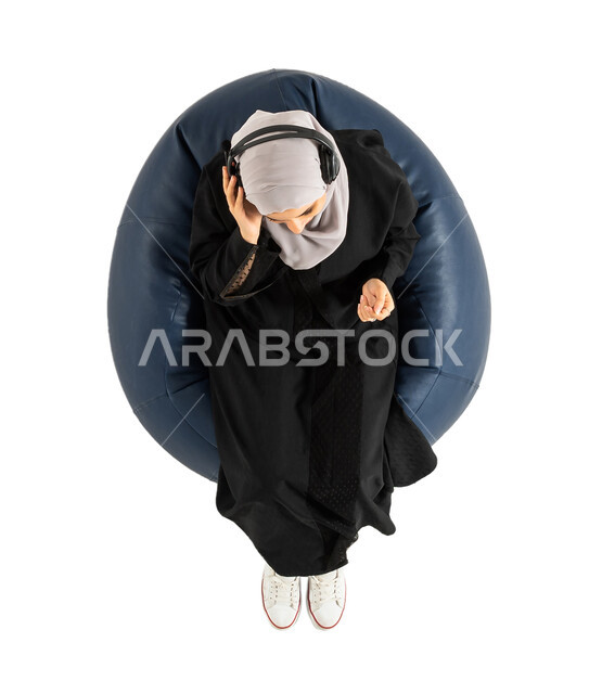 تقديم البرامج الاذاعية، تسجيل الاغاني والصوتيات، بورتريه لصورة علوية عامودية لأمرأة عربية خليجية سعودية تجلس على كرسي مريح، سيدة تضع سماعة الرأس ومستمتعة بسماع الاغاني والموسيقى،  التعليق الصوتي،غناء وطرب، موهبة وفن، خلفية بيضاء