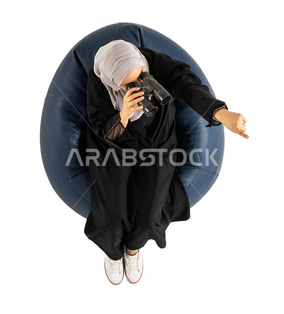 فريق الكشافة، رؤية مستقبلية، الاستكشاف والمغامرة، بورتريه لصورة علوية عامودية لأمرأة عربية خليجية سعودية تجلس على كرسي مريح وتنظر من خلال منظار الرؤية،  التخطيط المستقبلي، رؤية الاشياء البعيدة، خلفية بيضاء