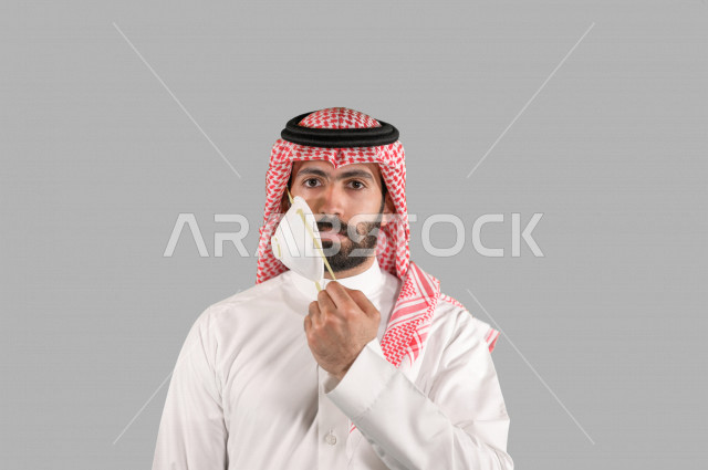 بورتريه لشاب عربي خليجي سعودي يقوم بإزالة الكمامة الواقية، اتخاذ اجراءات الوقاية من فايروس كورونا (كوفيد-19)، خلفية بيضاء