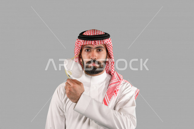 بورتريه لشاب عربي خليجي سعودي يقوم بإزالة الكمامة الواقية، اتخاذ اجراءات الوقاية من فايروس كورونا (كوفيد-19)، خلفية بيضاء