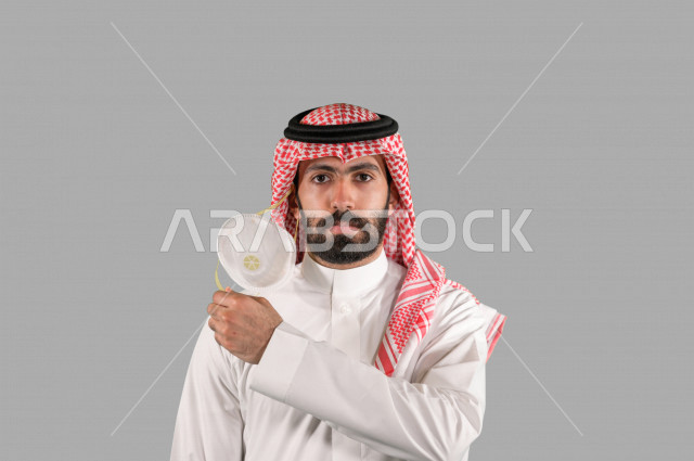 بورتريه لشاب عربي خليجي سعودي يقوم بإزالة الكمامة الواقية، اتخاذ اجراءات الوقاية من فايروس كورونا (كوفيد-19)، خلفية بيضاء