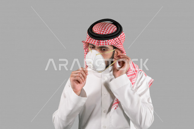 بورتريه لشاب عربي خليجي سعودي يقوم بإزالة الكمامة الواقية، اتخاذ اجراءات الوقاية من فايروس كورونا (كوفيد-19)، خلفية بيضاء