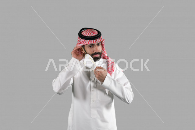 بورتريه لشاب عربي خليجي سعودي يقوم بإزالة الكمامة الواقية، اتخاذ اجراءات الوقاية من فايروس كورونا (كوفيد-19)، خلفية بيضاء