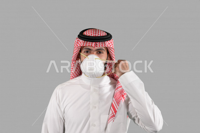 بورتريه لشاب عربي خليجي سعودي يقوم بإزالة الكمامة الواقية، اتخاذ اجراءات الوقاية من فايروس كورونا (كوفيد-19)، خلفية بيضاء