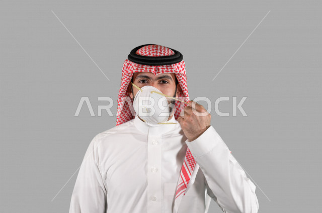 بورتريه لشاب عربي خليجي سعودي يقوم بإزالة الكمامة الواقية، اتخاذ اجراءات الوقاية من فايروس كورونا (كوفيد-19)، خلفية بيضاء