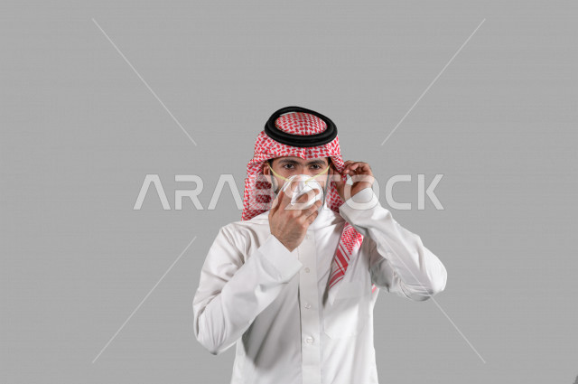 بورتريه لشاب عربي خليجي سعودي يقوم بإزالة الكمامة الواقية، اتخاذ اجراءات الوقاية من فايروس كورونا (كوفيد-19)، خلفية بيضاء