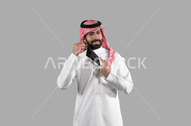 بورتريه لشاب عربي خليجي سعودي يقوم بإزالة الكمامة الواقية، اتخاذ اجراءات الوقاية من فايروس كورونا (كوفيد-19)، خلفية بيضاء