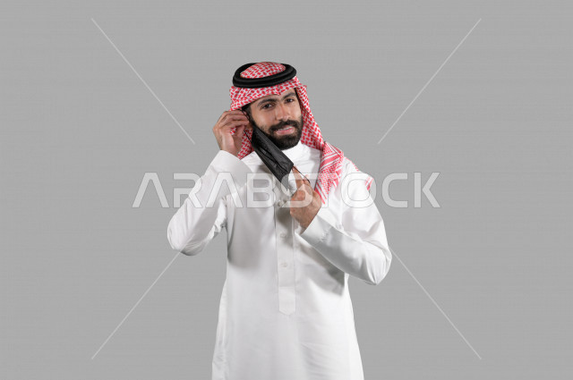 بورتريه لشاب عربي خليجي سعودي يقوم بإزالة الكمامة الواقية، اتخاذ اجراءات الوقاية من فايروس كورونا (كوفيد-19)، خلفية بيضاء