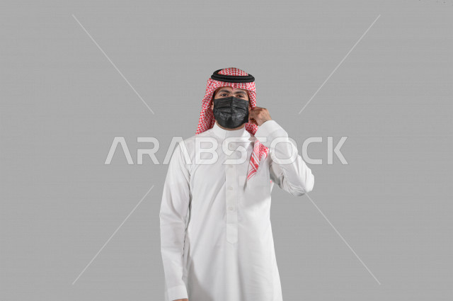 بورتريه لشاب عربي خليجي سعودي يقوم بإزالة الكمامة الواقية، اتخاذ اجراءات الوقاية من فايروس كورونا (كوفيد-19)، خلفية بيضاء