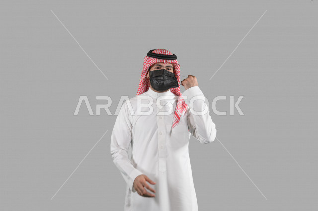 بورتريه لشاب عربي خليجي سعودي يقوم بإزالة الكمامة الواقية، اتخاذ اجراءات الوقاية من فايروس كورونا (كوفيد-19)، خلفية بيضاء