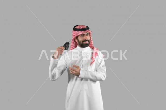 بورتريه لشاب عربي خليجي سعودي يقوم بإزالة الكمامة الواقية، اتخاذ اجراءات الوقاية من فايروس كورونا (كوفيد-19)، خلفية بيضاء