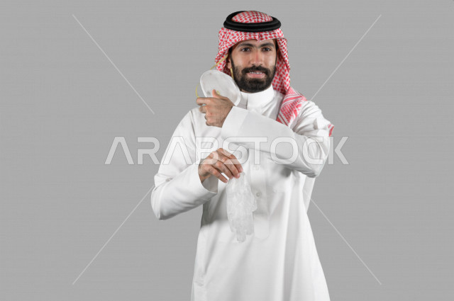 بورتريه لشاب عربي خليجي سعودي يمسك بيده قفازات ويقوم بإزالة الكمامة الواقية، اتخاذ اجراءات الوقاية من فايروس كورونا (كوفيد-19)، خلفية بيضاء
