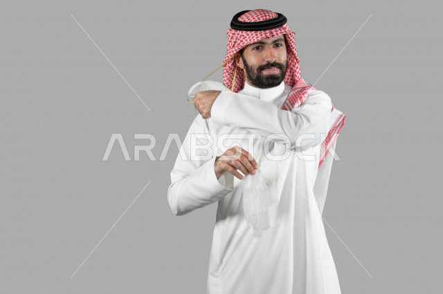 بورتريه لشاب عربي خليجي سعودي يمسك بيده قفازات ويقوم بإزالة الكمامة الواقية، اتخاذ اجراءات الوقاية من فايروس كورونا (كوفيد-19)، خلفية بيضاء