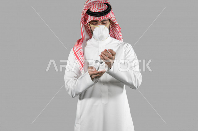بورتريه لشاب عربي خليجي سعودي، ارتداء الكمامة الواقية، اتخاذ اجراءات الوقاية من فايروس كورونا (كوفيد-19)، استخدام معقم اليدين، تعقيم اليدين، تجنب انتشار العدوى، خلفية بيضاء