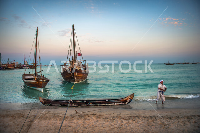 رجل عربي خليجي قطري على شاطئ كتارا في الدوحة بقطر، كورنيش الدوحة، القوارب الخشبية، علم قطر، السياحة في قطر