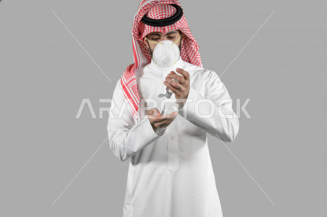 بورتريه لشاب عربي خليجي سعودي، ارتداء الكمامة الواقية، اتخاذ اجراءات الوقاية من فايروس كورونا (كوفيد-19)، استخدام معقم اليدين، تعقيم اليدين، تجنب انتشار العدوى، خلفية بيضاء