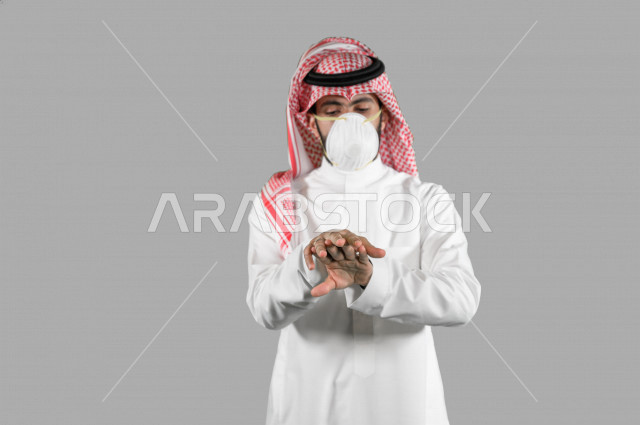 بورتريه لشاب عربي خليجي سعودي، ارتداء الكمامة الواقية، اتخاذ اجراءات الوقاية من فايروس كورونا (كوفيد-19)، استخدام معقم اليدين، تعقيم اليدين، تجنب انتشار العدوى، خلفية بيضاء