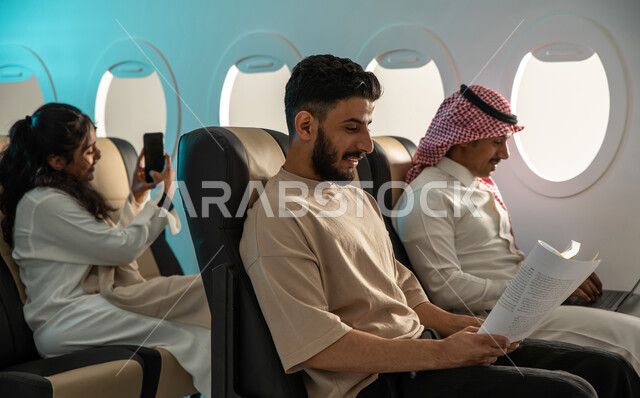  رحلة جوية سياحية ممتعة ، التقاط صور تذكارية باستخدام الهاتف المحمول  ، مجموعة من الركاب  العرب الخليجيون السعوديون في مقصورة  الطائرة ،  الاستمتاع بالقراءة على متن الطائرة.