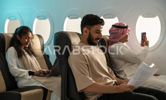 Taking souvenir photos on the plane, a group of Saudi Gulf Arab passengers on the plane, Saudi Airlines, tourism and travel, completing work tasks via a laptop, reading useful books for learning and culture.