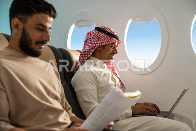 الاستمتاع بالقراءة على متن الطائرة ،  رجلان عربيان خليجيان سعوديان في مقعد الطائرة ، رحلة عمل ، الخطوط الجوية السعودية  ، انجاز مهام العمل عبر  جهاز الحاسوب  المحمول ، درجة رجال الاعمال .